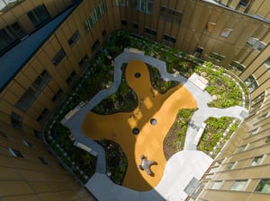 Luftfoto av indre gårdsrom ved Nye Stavanger Universitetssjukehus med grønne planter, sittebenker og skulptur.